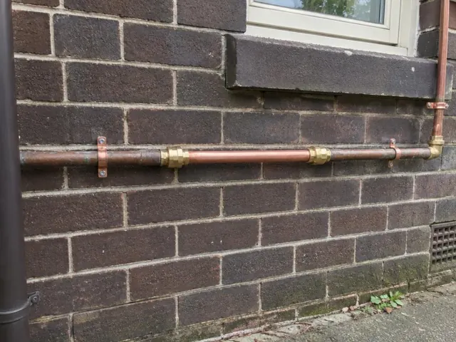 Repaired copper water pipe on a brick house exterior wall near a window in Waverley