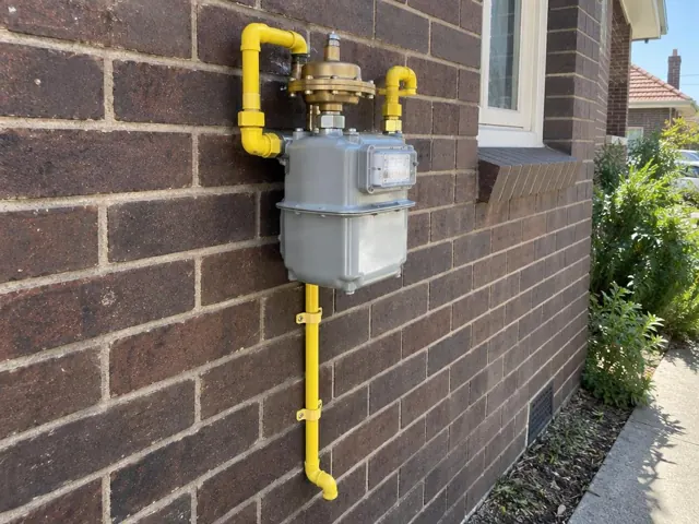Yellow gas meter and pipework on a brick exterior wall in Bronte